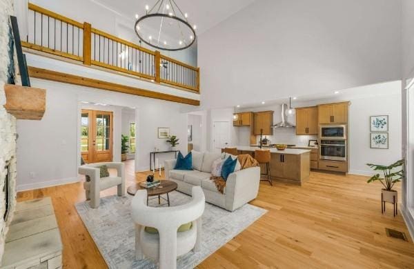 living room featuring french doors, a chandelier, light wood-type flooring, a towering ceiling, and a fireplace