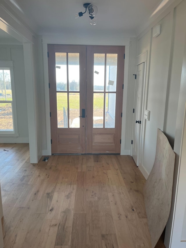 doorway with crown molding, french doors, and light wood-type flooring