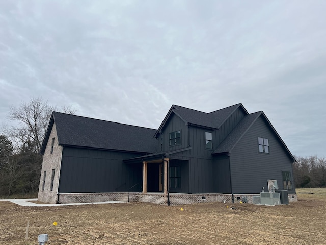 view of front facade featuring a shingled roof, brick siding, board and batten siding, and crawl space