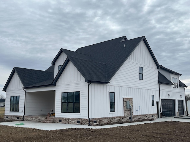 rear view of property featuring a shingled roof, board and batten siding, driveway, and crawl space