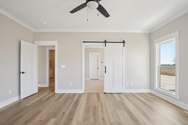 unfurnished bedroom featuring ornamental molding, light hardwood / wood-style floors, a barn door, and ceiling fan