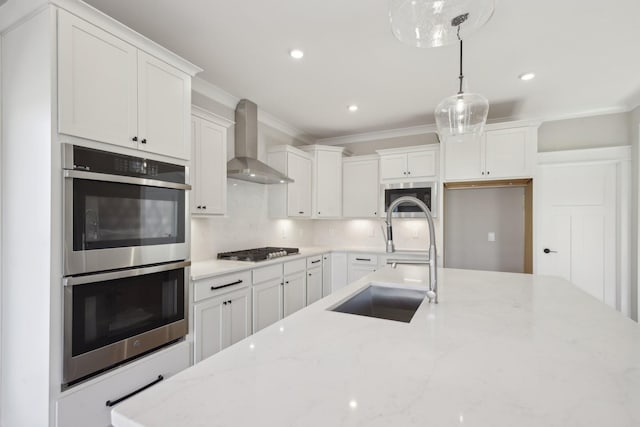 kitchen featuring wall chimney exhaust hood, sink, decorative light fixtures, stainless steel appliances, and white cabinets