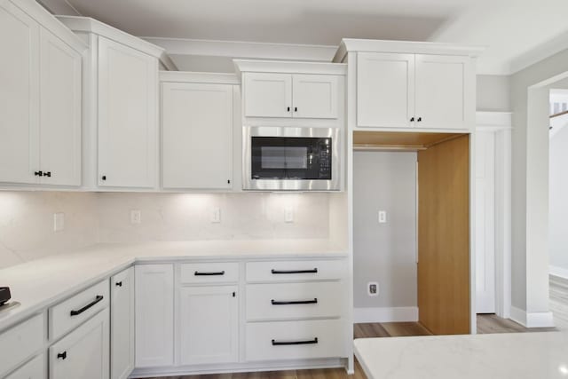 kitchen with white cabinetry, stainless steel microwave, light hardwood / wood-style floors, and tasteful backsplash