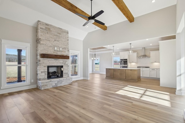 unfurnished living room with ceiling fan with notable chandelier, high vaulted ceiling, light hardwood / wood-style floors, a stone fireplace, and beamed ceiling