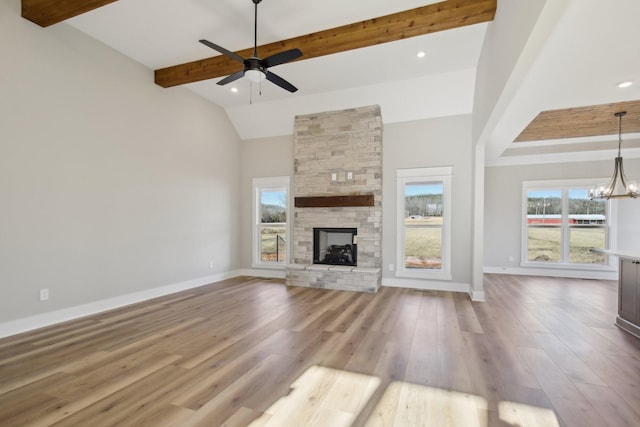 unfurnished living room with ceiling fan with notable chandelier, high vaulted ceiling, a stone fireplace, beamed ceiling, and light wood-type flooring