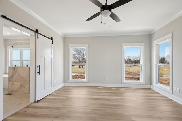 empty room featuring ornamental molding, a barn door, ceiling fan, and light hardwood / wood-style floors