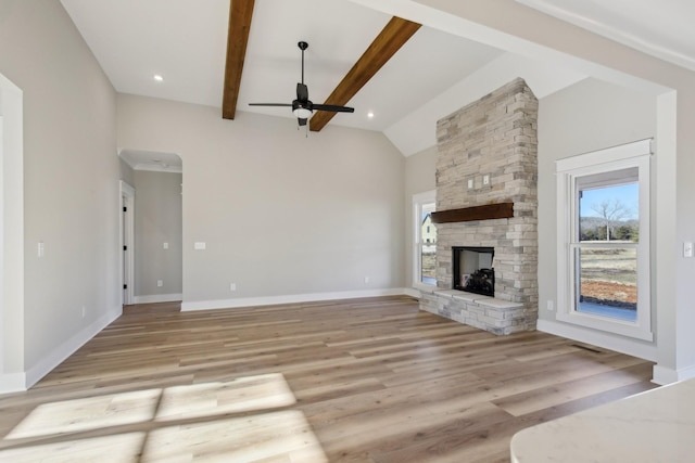 unfurnished living room featuring lofted ceiling with beams, a stone fireplace, ceiling fan, and light hardwood / wood-style flooring