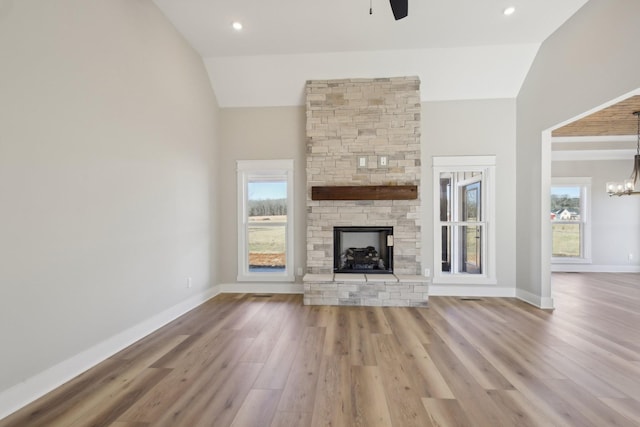 unfurnished living room featuring light hardwood / wood-style flooring, a stone fireplace, vaulted ceiling, and ceiling fan with notable chandelier