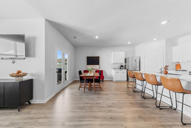 kitchen with white cabinetry, stainless steel fridge, light hardwood / wood-style floors, and a breakfast bar area