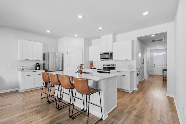 kitchen with appliances with stainless steel finishes, a kitchen island with sink, sink, and white cabinets