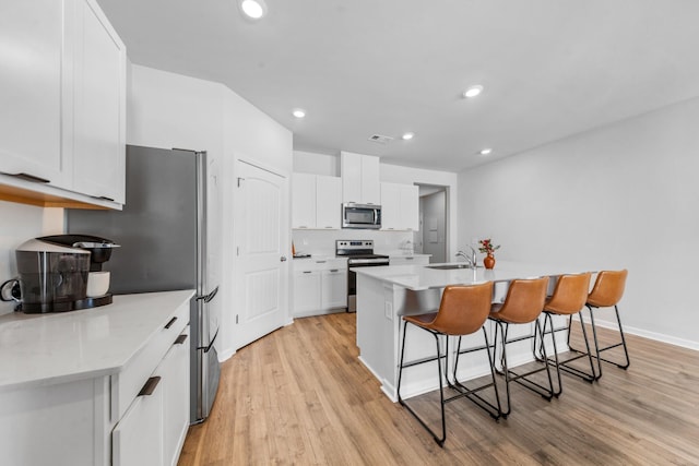 kitchen featuring light wood-type flooring, a kitchen breakfast bar, stainless steel appliances, a kitchen island with sink, and white cabinets