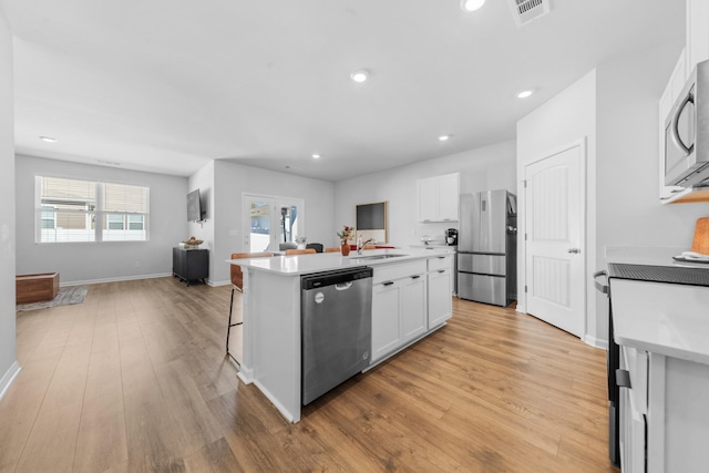 kitchen with appliances with stainless steel finishes, a breakfast bar, white cabinetry, a center island with sink, and light wood-type flooring