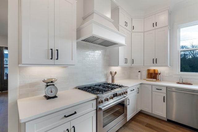 kitchen featuring premium range hood, hardwood / wood-style floors, tasteful backsplash, white cabinetry, and stainless steel appliances