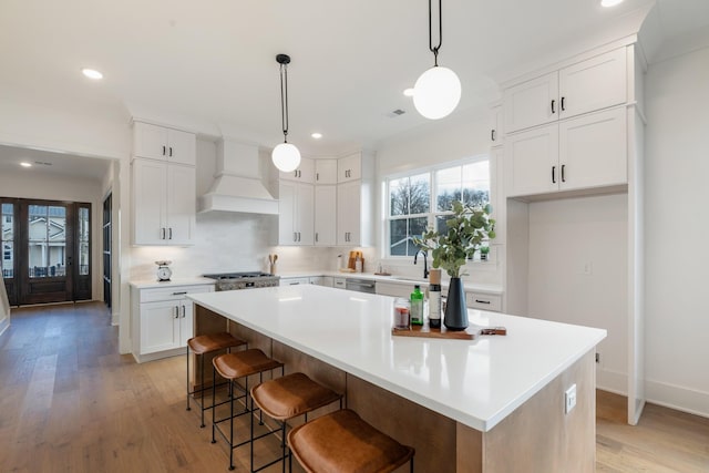 kitchen with a center island, white cabinets, a kitchen bar, decorative light fixtures, and custom exhaust hood