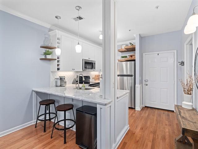 kitchen with appliances with stainless steel finishes, white cabinets, hanging light fixtures, kitchen peninsula, and light hardwood / wood-style flooring