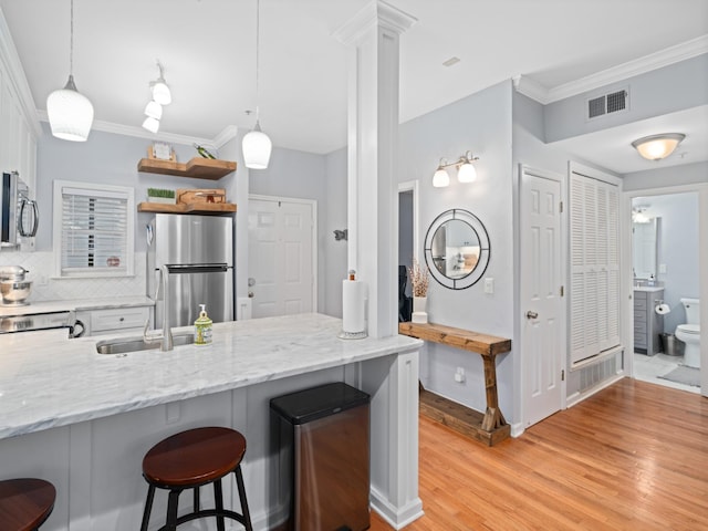 kitchen with a kitchen bar, hanging light fixtures, kitchen peninsula, stainless steel appliances, and light stone countertops