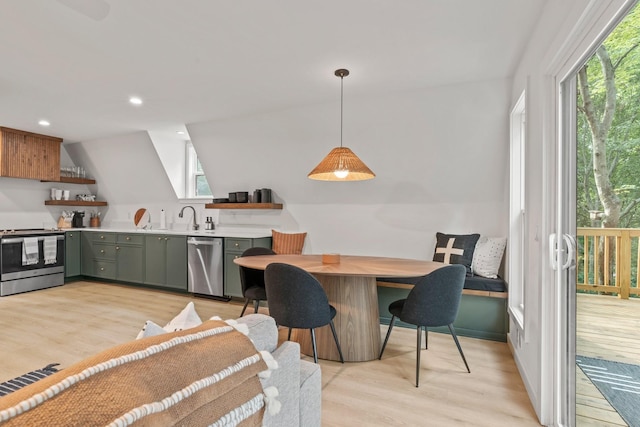 kitchen with green cabinets, appliances with stainless steel finishes, decorative light fixtures, and light hardwood / wood-style floors