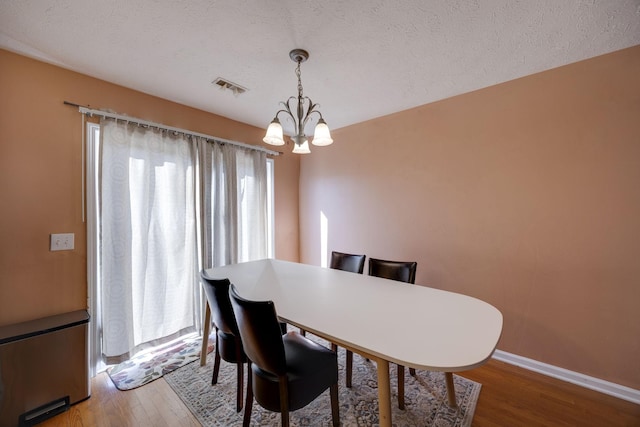 dining area featuring wood-type flooring, plenty of natural light, a textured ceiling, and an inviting chandelier