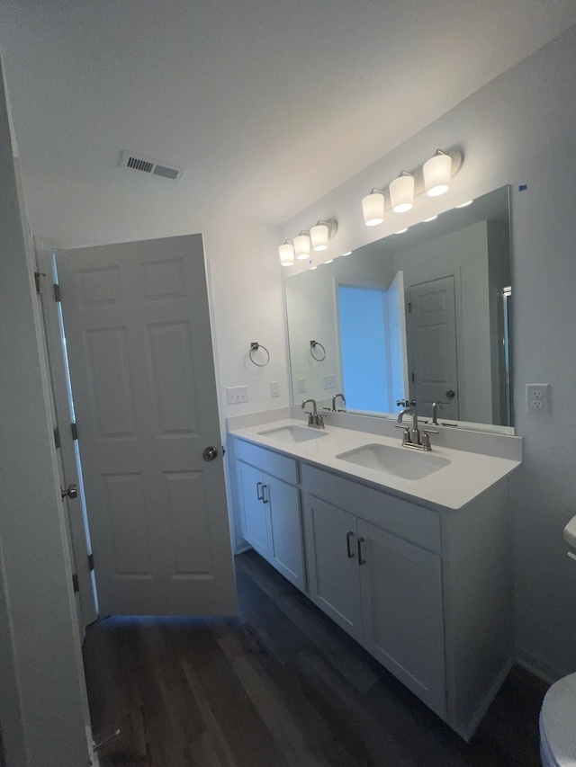 bathroom featuring visible vents, toilet, double vanity, wood finished floors, and a sink