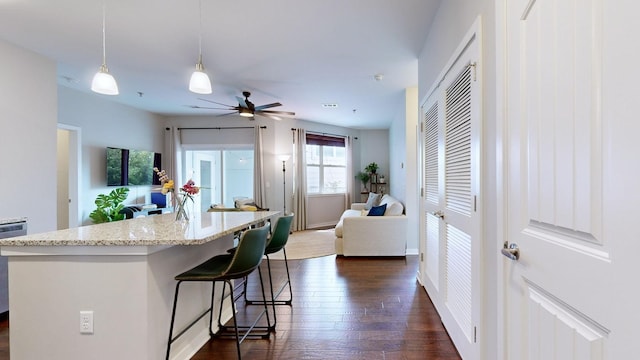 kitchen with a breakfast bar area, ceiling fan, dark hardwood / wood-style floors, an island with sink, and decorative light fixtures