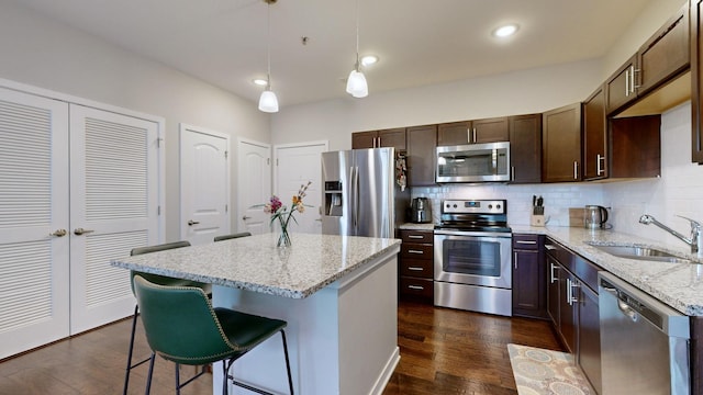 kitchen featuring pendant lighting, sink, appliances with stainless steel finishes, a center island, and light stone counters