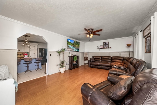 living room with crown molding, ceiling fan, a textured ceiling, and light wood-type flooring