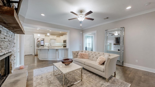 living room featuring wood-type flooring, a stone fireplace, sink, and ornamental molding