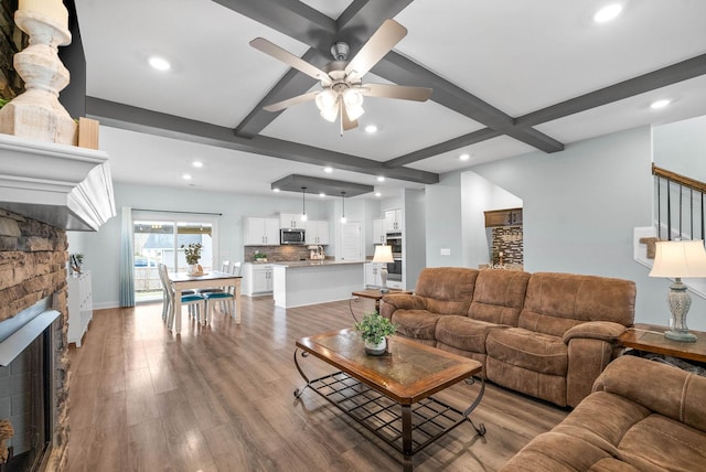 living room with beam ceiling, a stone fireplace, light hardwood / wood-style floors, and ceiling fan