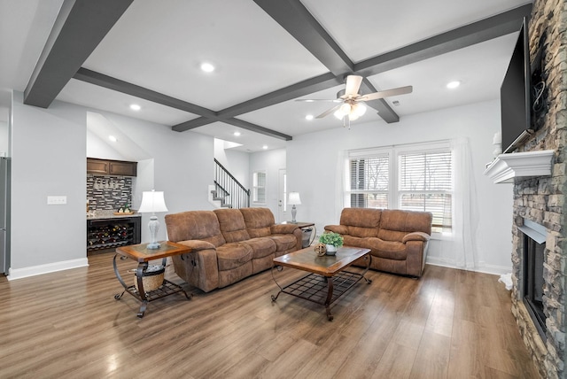 living room with beamed ceiling, bar area, a stone fireplace, and light wood-type flooring