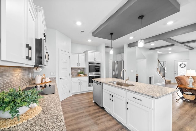 kitchen with sink, pendant lighting, stainless steel appliances, light stone countertops, and white cabinets