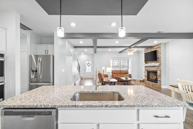 kitchen with appliances with stainless steel finishes, white cabinetry, hanging light fixtures, light stone countertops, and an island with sink