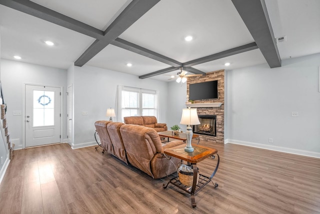 living room with beamed ceiling, a stone fireplace, hardwood / wood-style floors, and ceiling fan