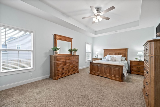 bedroom featuring ceiling fan, a tray ceiling, and light carpet