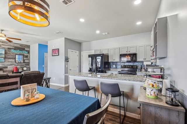 kitchen with sink, light stone counters, black appliances, dark hardwood / wood-style flooring, and wood walls