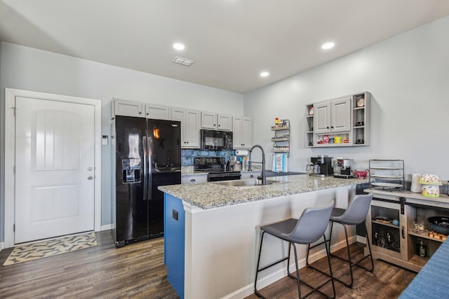 kitchen with dark wood-type flooring, a kitchen bar, sink, light stone counters, and black appliances