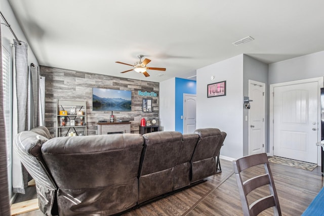 living room with hardwood / wood-style flooring, a large fireplace, wooden walls, and ceiling fan