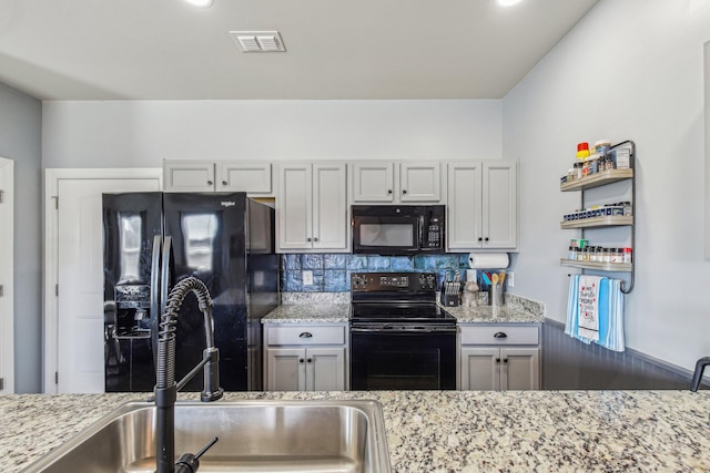 kitchen with tasteful backsplash, sink, light stone counters, and black appliances