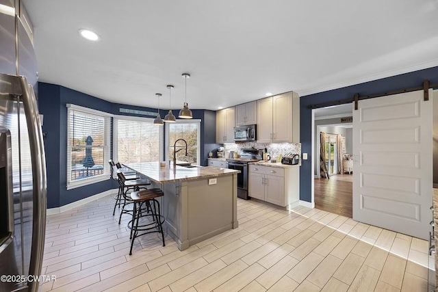 kitchen with pendant lighting, gray cabinetry, stainless steel appliances, a barn door, and a center island with sink