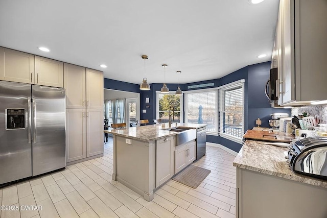 kitchen featuring light stone countertops, appliances with stainless steel finishes, pendant lighting, and a center island with sink