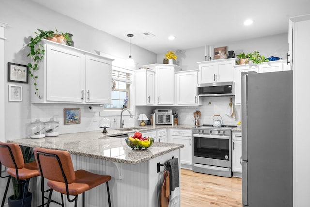 kitchen with pendant lighting, appliances with stainless steel finishes, kitchen peninsula, and white cabinets