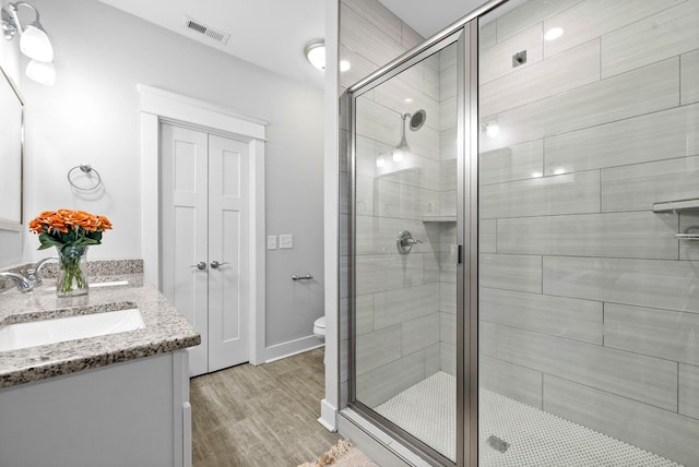 bathroom with hardwood / wood-style flooring, vanity, an enclosed shower, and toilet