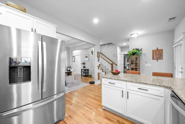 kitchen with white cabinetry, light stone counters, light hardwood / wood-style flooring, and appliances with stainless steel finishes