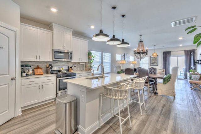 kitchen featuring sink, appliances with stainless steel finishes, a kitchen island with sink, white cabinets, and decorative light fixtures