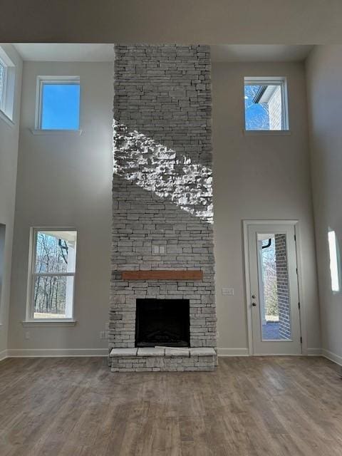 unfurnished living room with wood-type flooring, a stone fireplace, and a towering ceiling