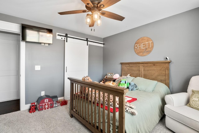 carpeted bedroom featuring a barn door and ceiling fan