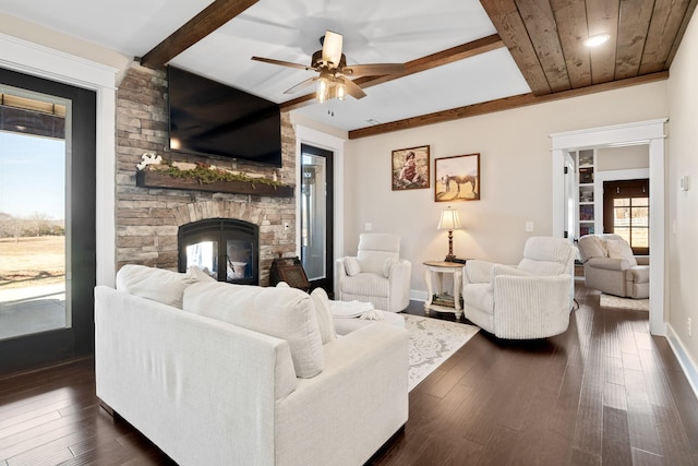 living room with beamed ceiling, a stone fireplace, dark hardwood / wood-style floors, and ceiling fan