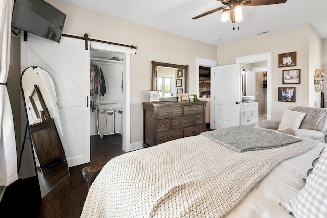 bedroom with a spacious closet, ceiling fan, a barn door, dark wood-type flooring, and a closet