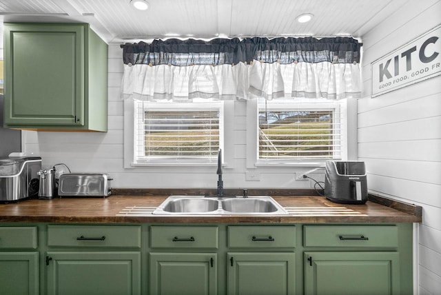 kitchen with sink, a wealth of natural light, wooden walls, and green cabinets