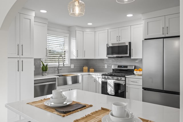 kitchen with white cabinetry, sink, decorative backsplash, hanging light fixtures, and stainless steel appliances