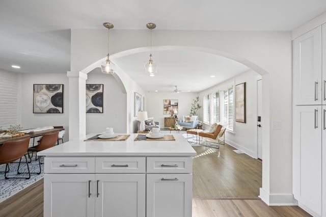 kitchen with white cabinetry, hanging light fixtures, light hardwood / wood-style flooring, a kitchen island, and ceiling fan